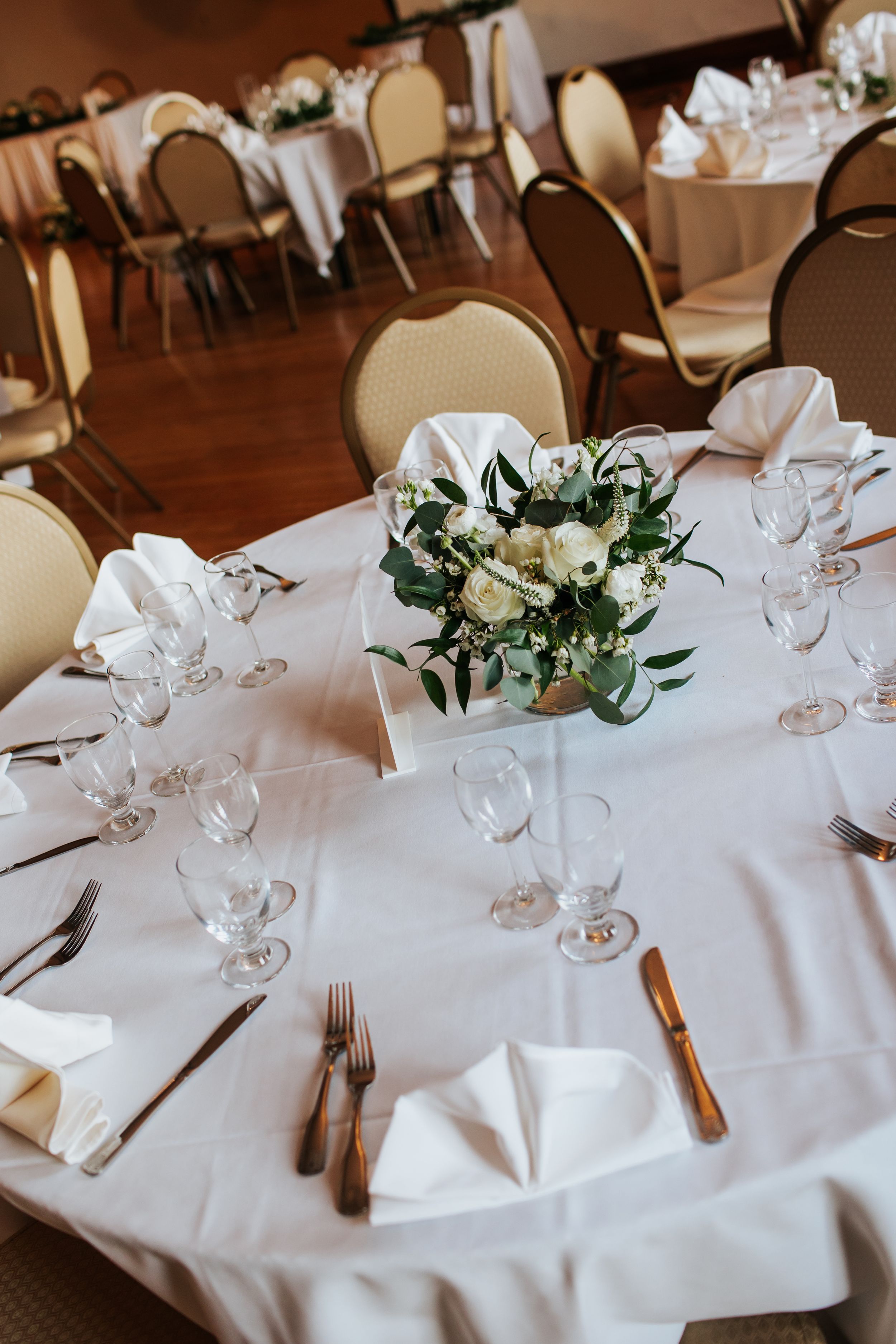 Elegant wedding reception tables with white linens, wine glasses, and delicate floral centerpieces in a rustic venue.