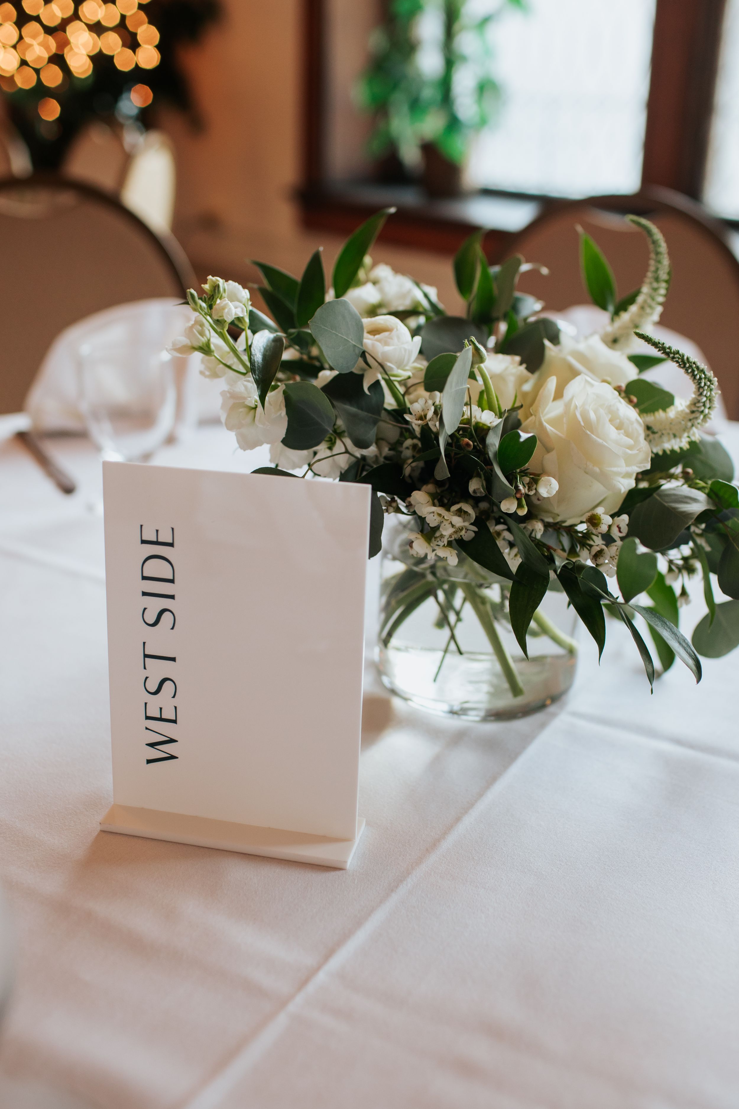 White floral centerpieces with table numbers displayed on elegant place cards at an upscale wedding reception.