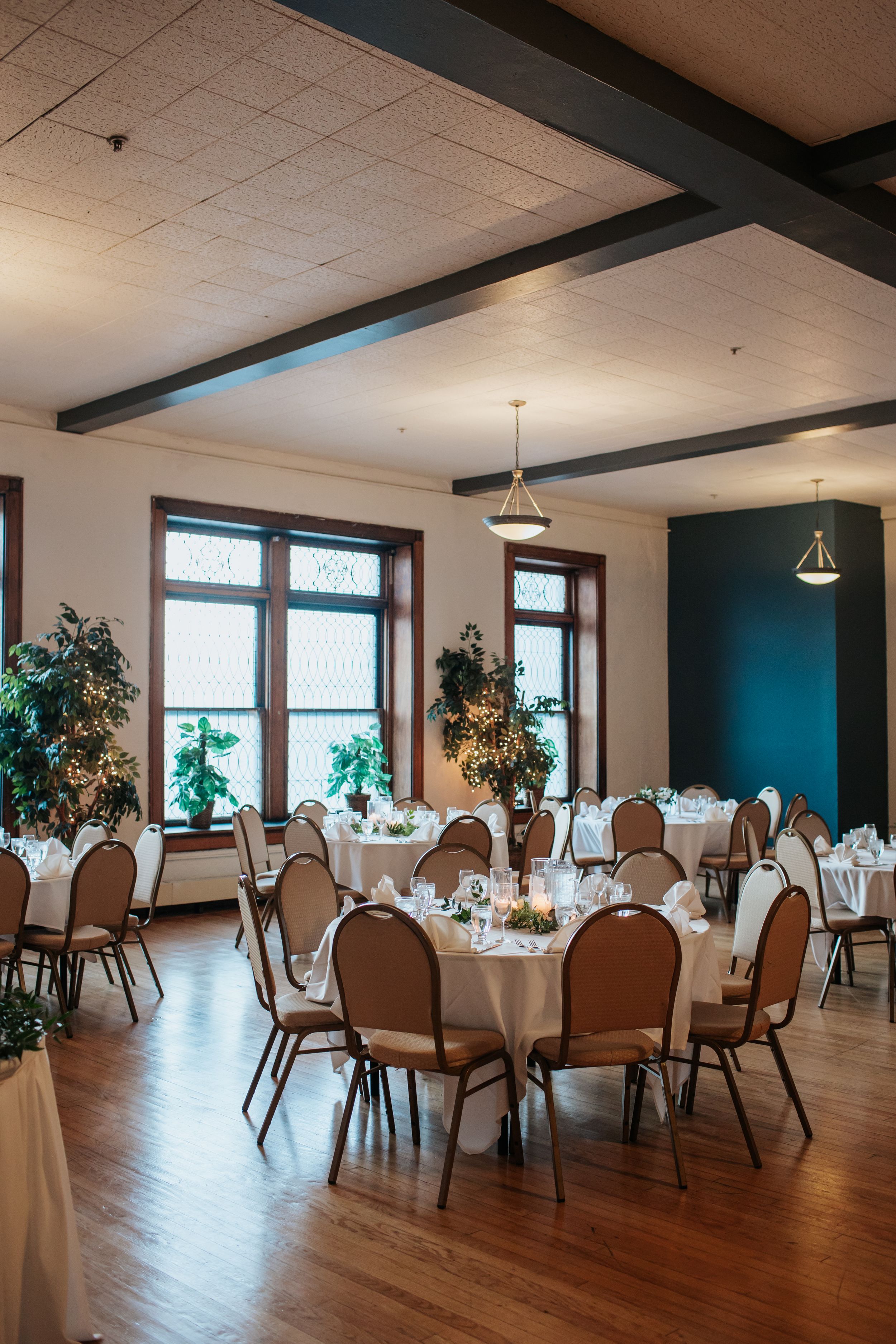 Panoramic view of an elegant banquet hall with round tables, brown chairs and teal accent walls prepared for dining.