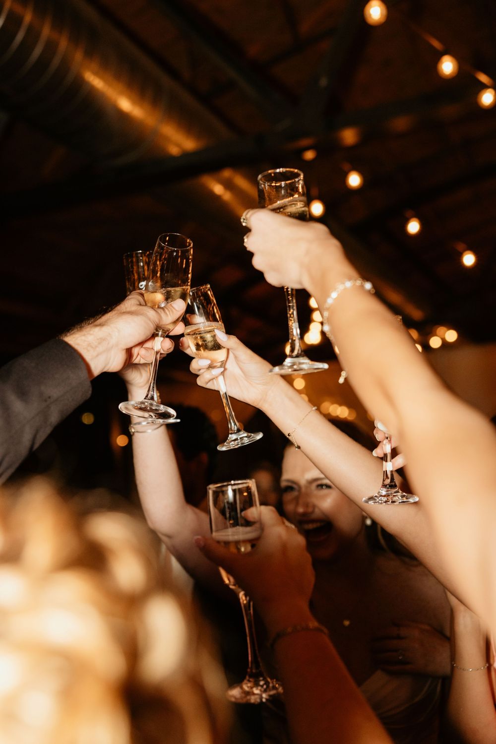 Raised champagne glasses toast in celebration with string lights glowing warmly in the background at Georgia wedding venue