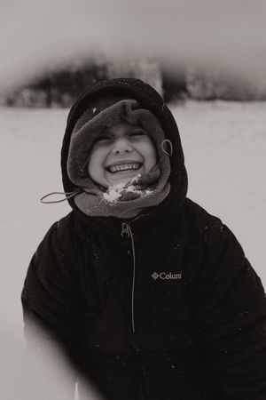 A series of close-up portraits showing a person wearing a black winter coat and hood while smiling in snowy weather.
