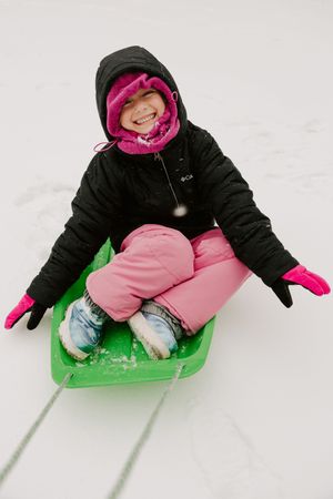 Someone wearing a black winter coat and pink pants slides down a snowy hill on a bright green sled.