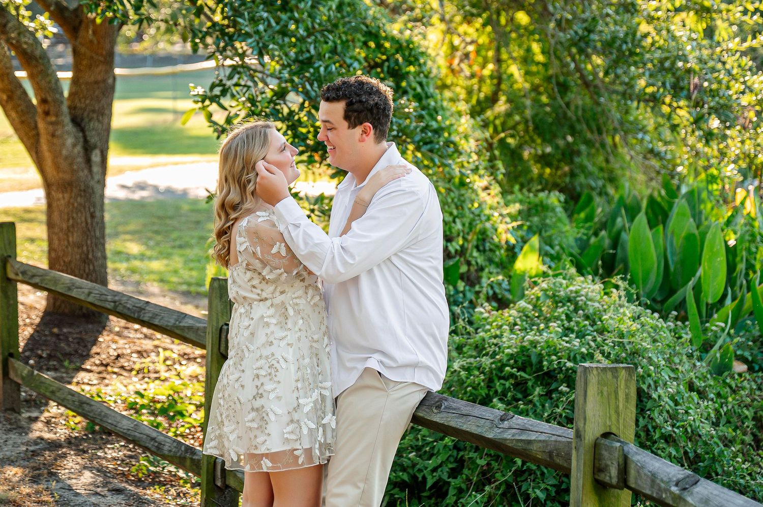 A couple poses together in a garden setting with natural sunlight filtering through trees.