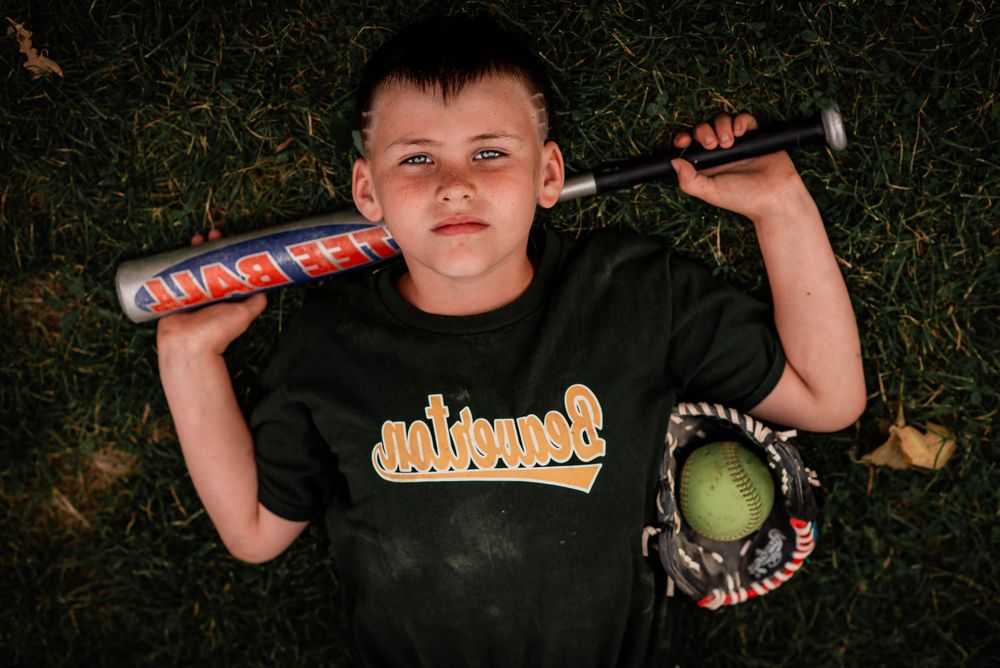 A young boy laying in the grass with his baseball gear in Beaverton, Ontario.