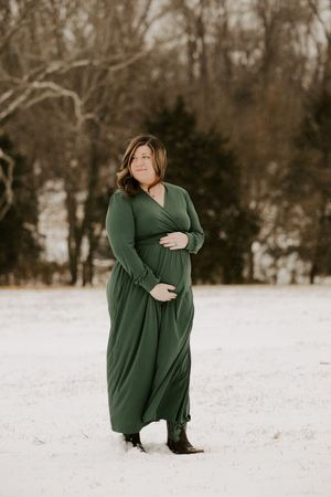 Person in a green sweater dress poses gracefully in a snowy winter landscape during an outdoor photoshoot.