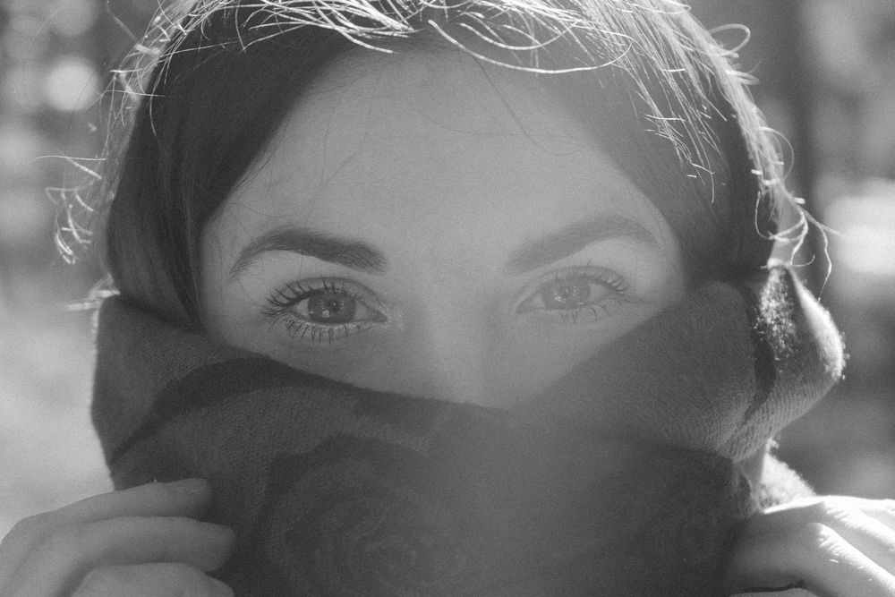 Black and white close-up portrait of a woman with expressive eyes, partially covering her face with a scarf.