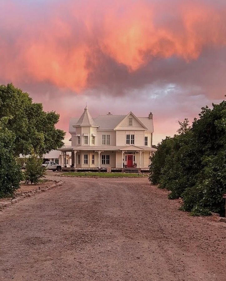White farmhouse on a hilltop with dramatic pink sunset clouds and dirt path leading to the entrance.