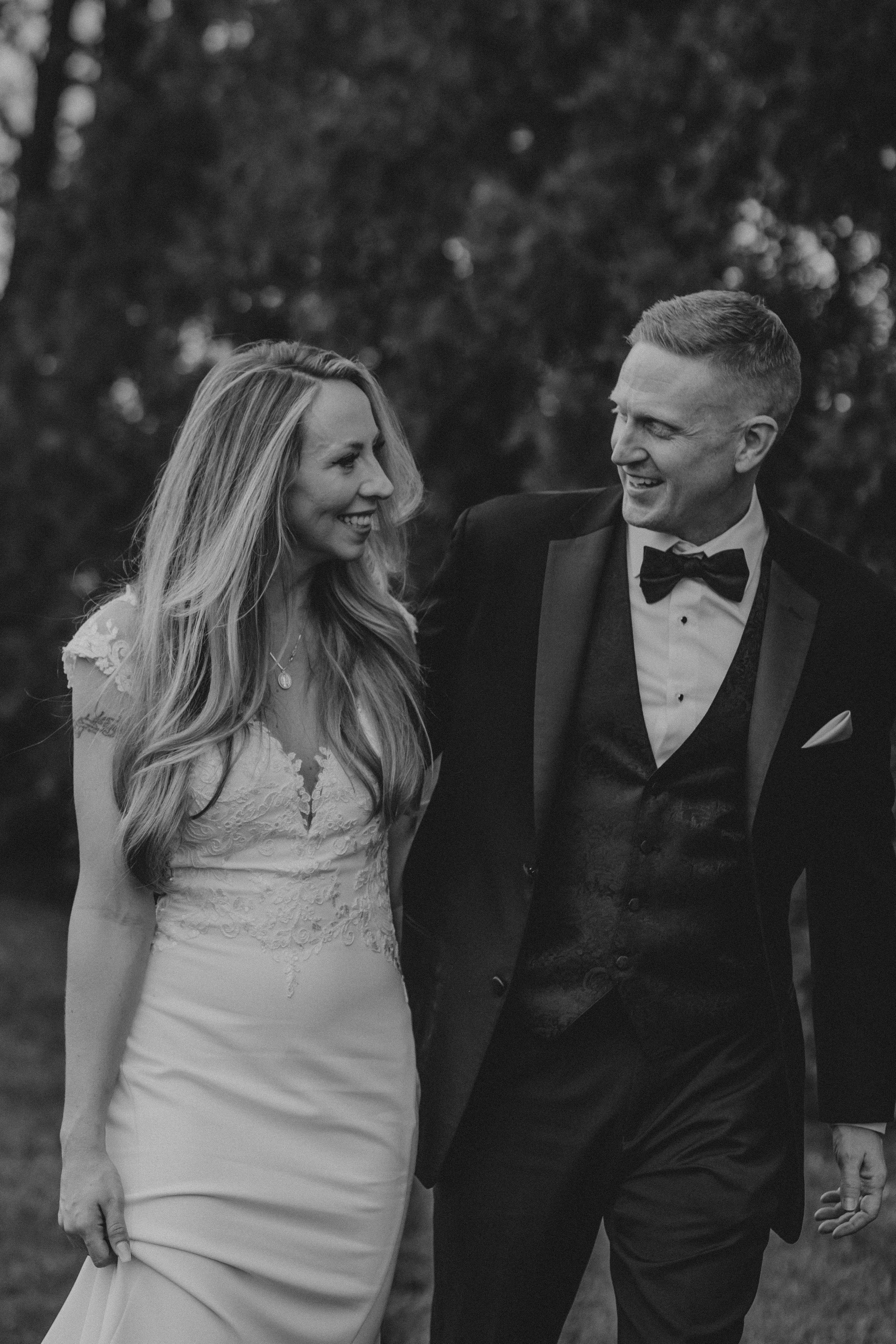 Black and white wedding photos show happy couple laughing together in formal attire during outdoor photoshoot.