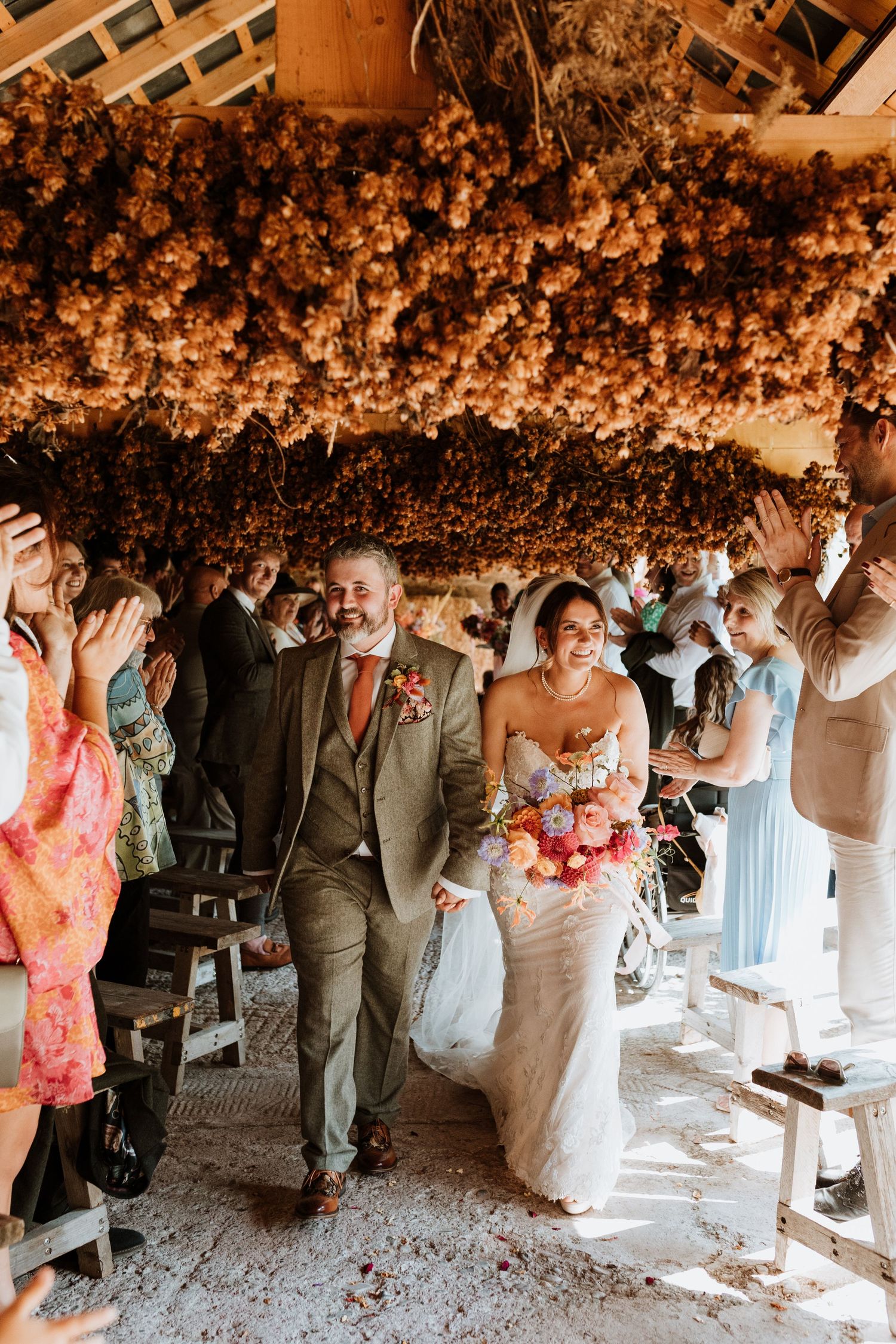 Wedding guests dancing and celebrating under a rustic stone archway decorated with floral arrangements.