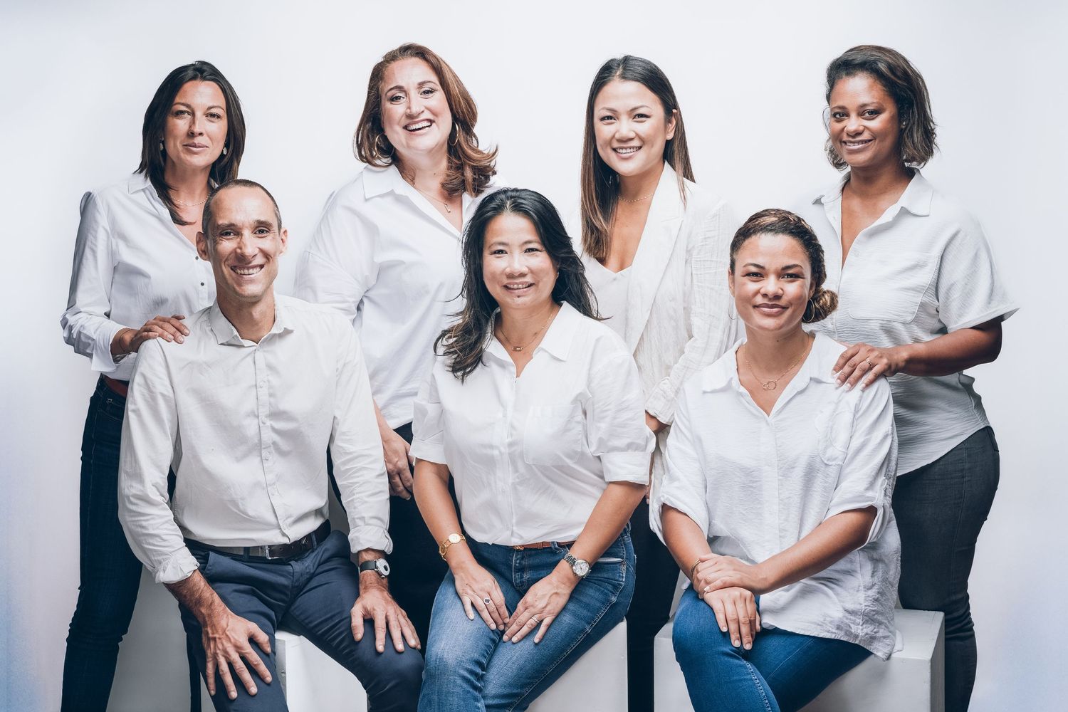 Diverse group of women wearing white tops smiling and laughing together in a casual studio setting.