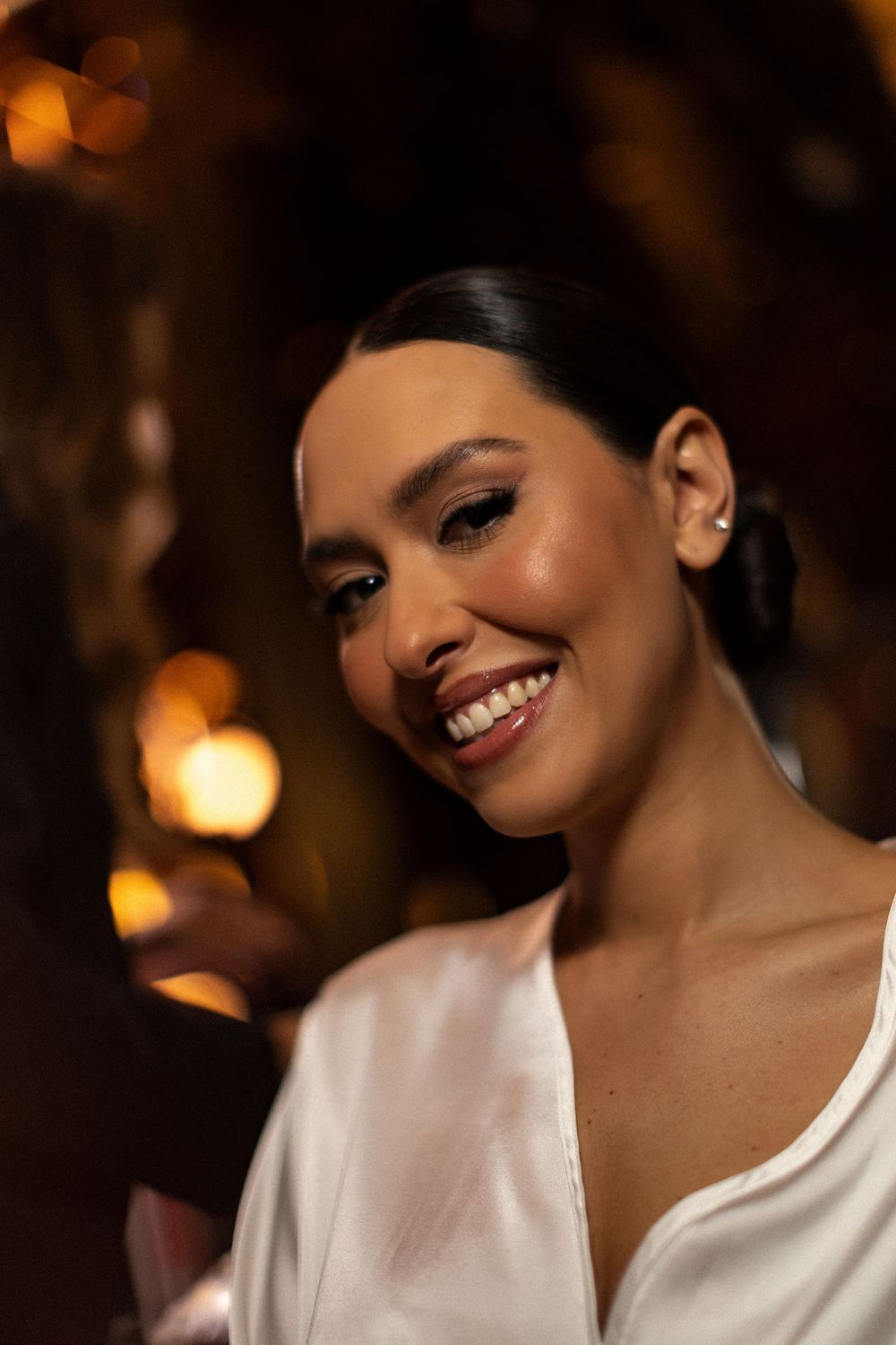 A glowing portrait shows a radiant smile in warm lighting wearing an elegant white top.