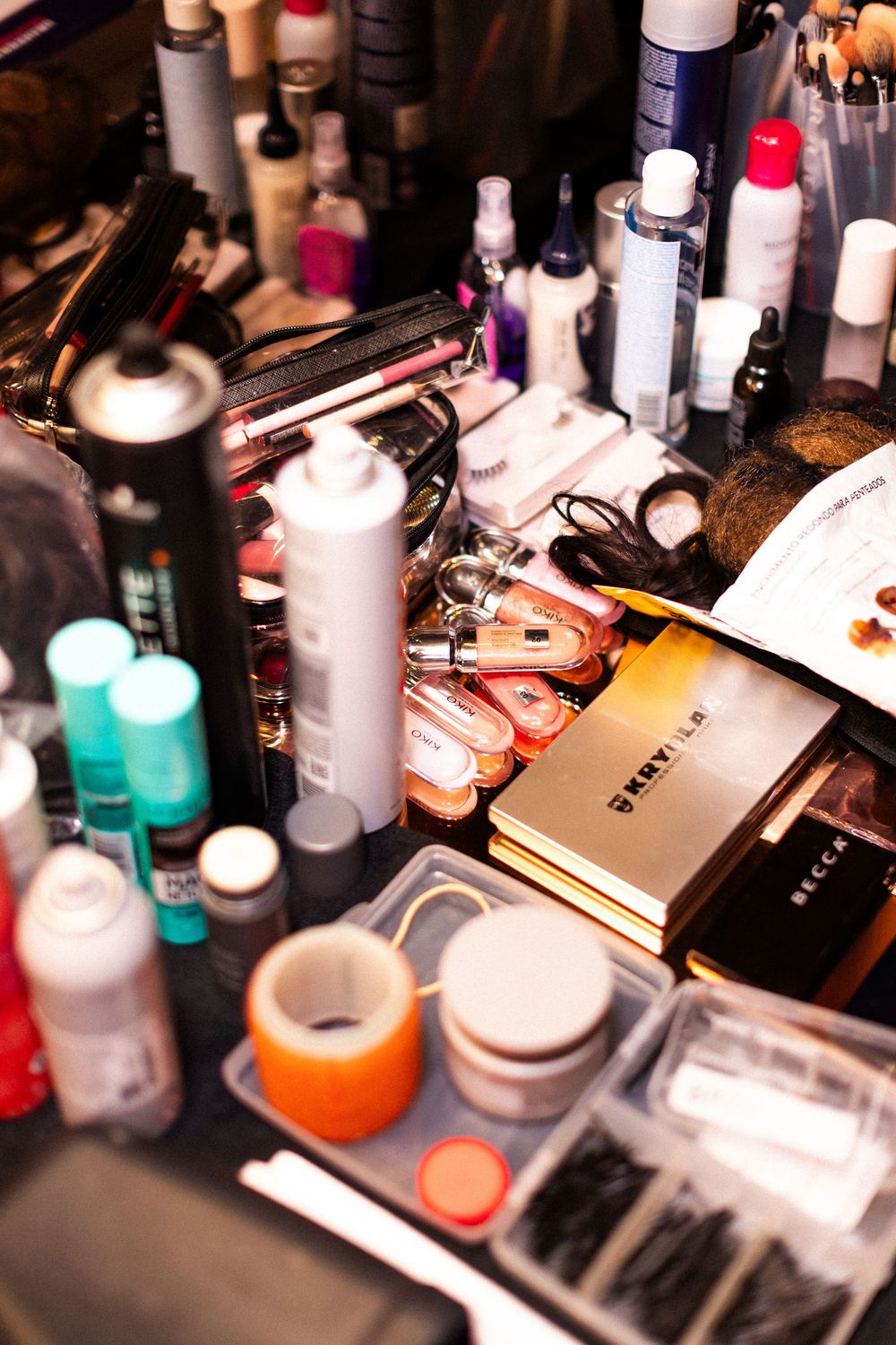 A cluttered makeup table displays various cosmetics, beauty products and tools in disarray.