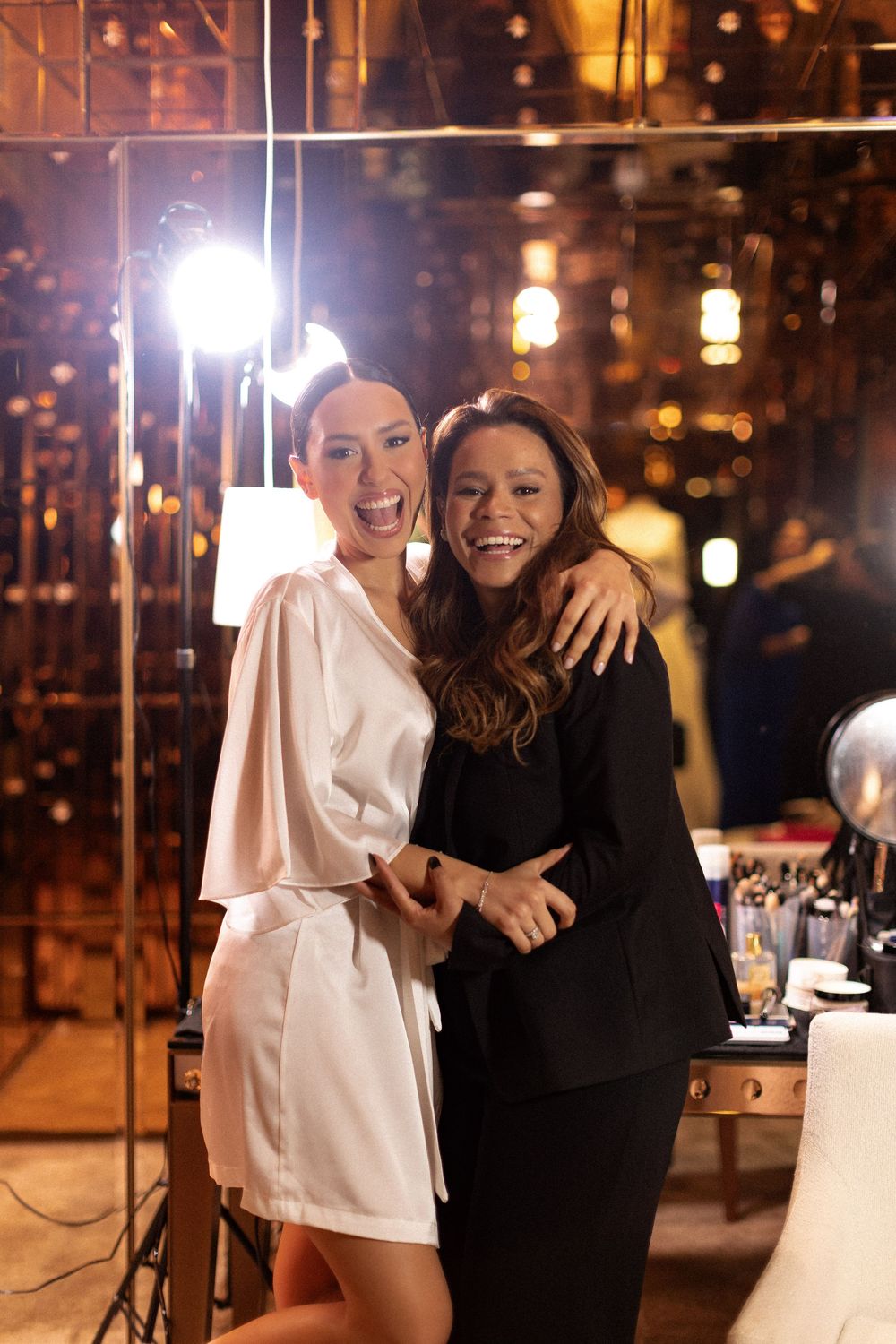 Two friends share a joyful moment together at a nighttime event with warm lighting and bokeh in the background.