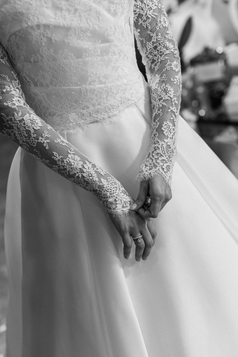 Close-up details of delicate white lace sleeves on a wedding dress against a light background.