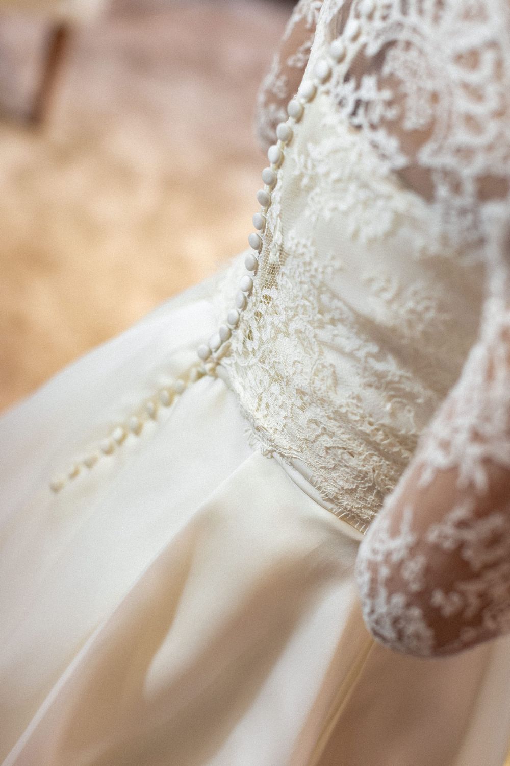 Close-up detail of delicate lace and button details on a white wedding dress.