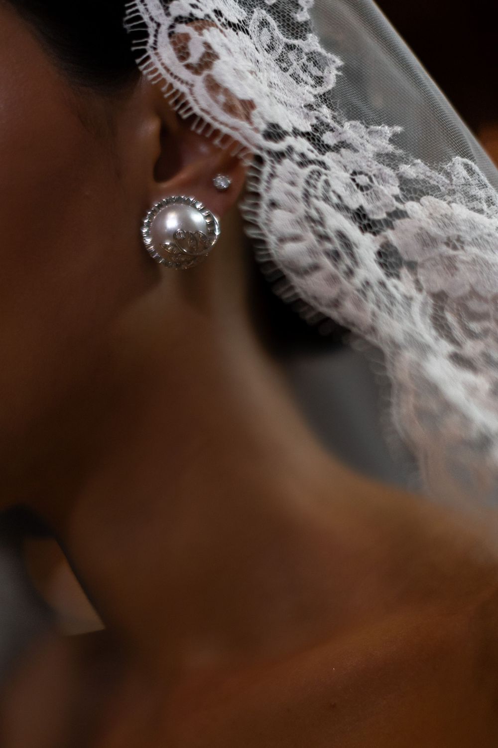 Close-up detail of delicate white lace trim on a wedding dress against a dark background.