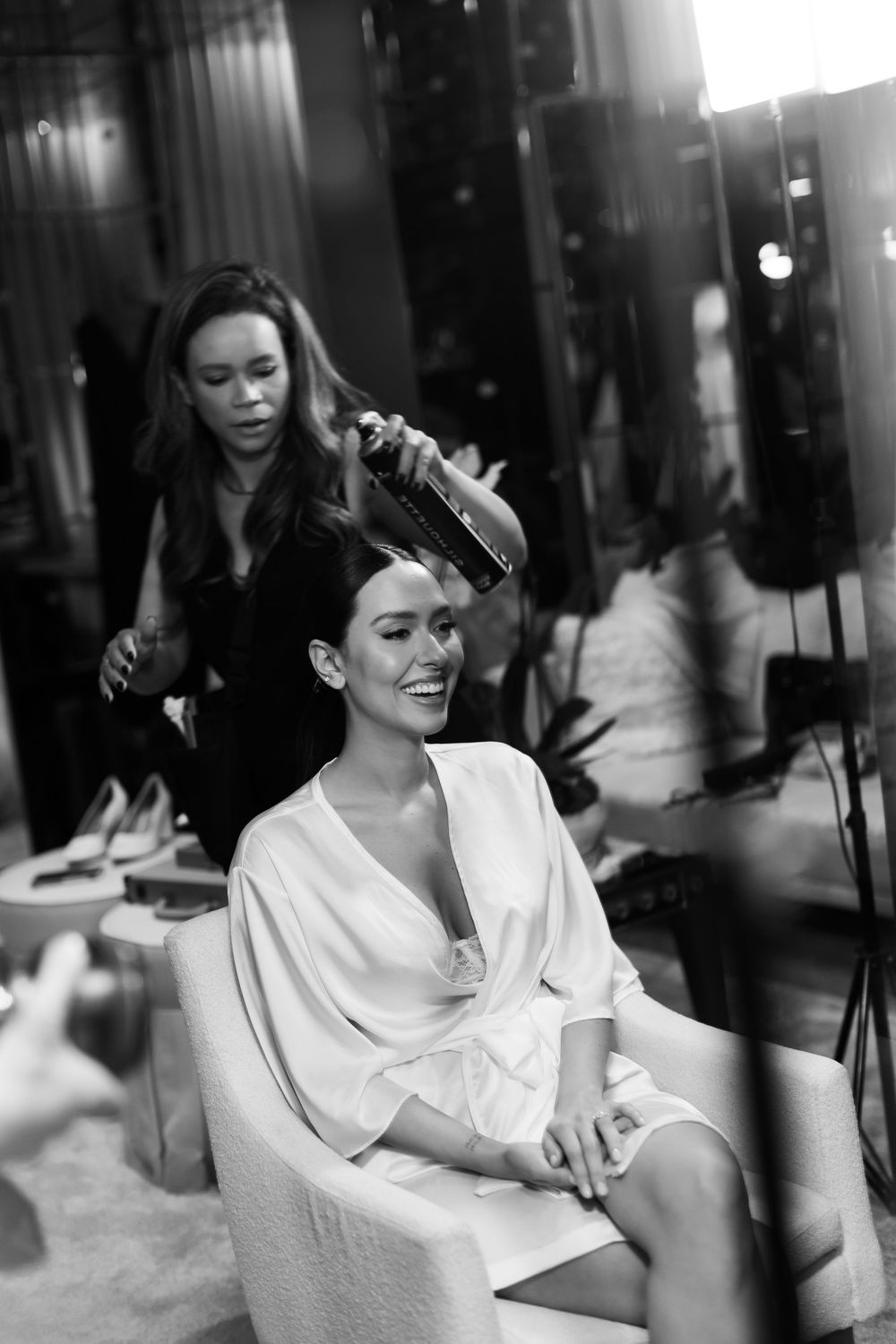 Woman in white robe laughing while getting ready in black and white photography.