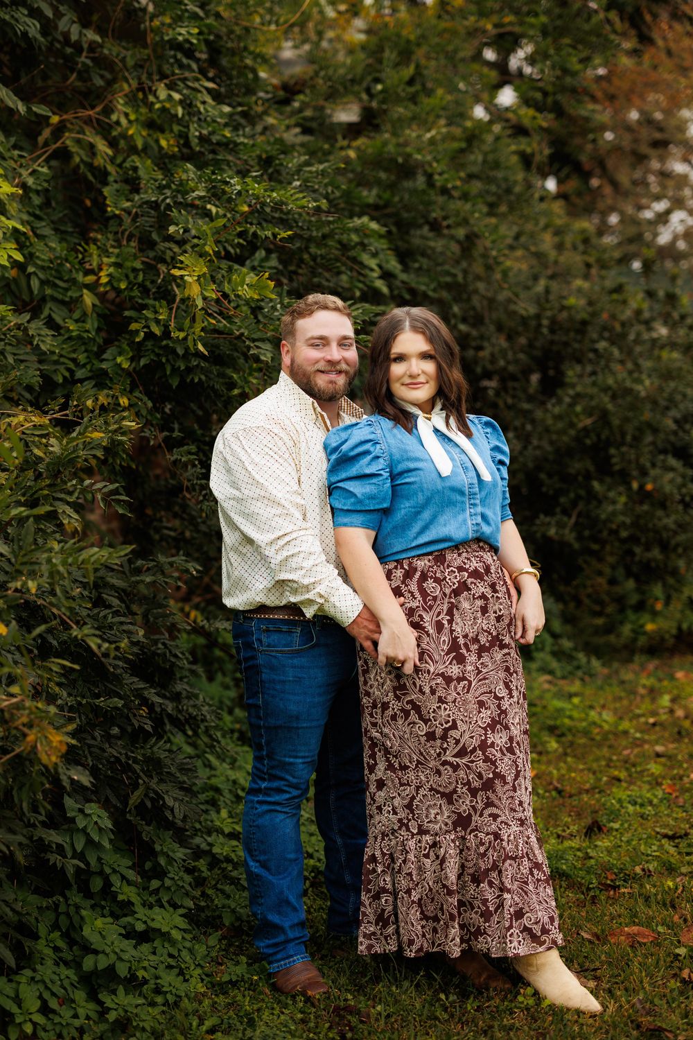A couple in denim and vintage-inspired clothing poses playfully in a garden setting.