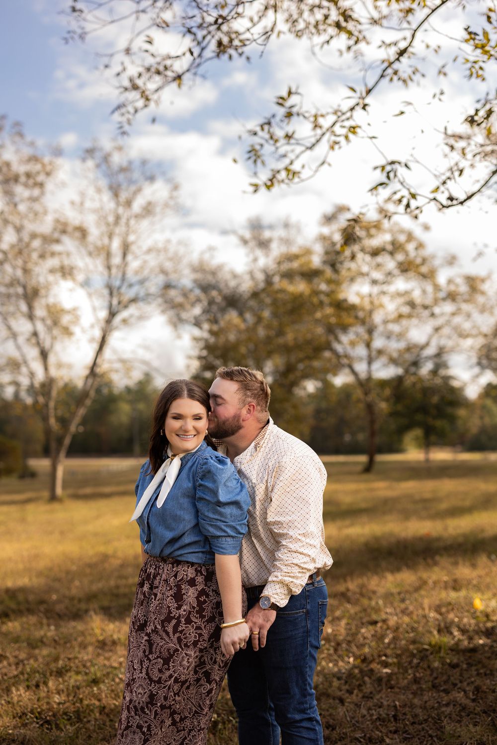 A couple shares an intimate moment in a sunlit autumn field.