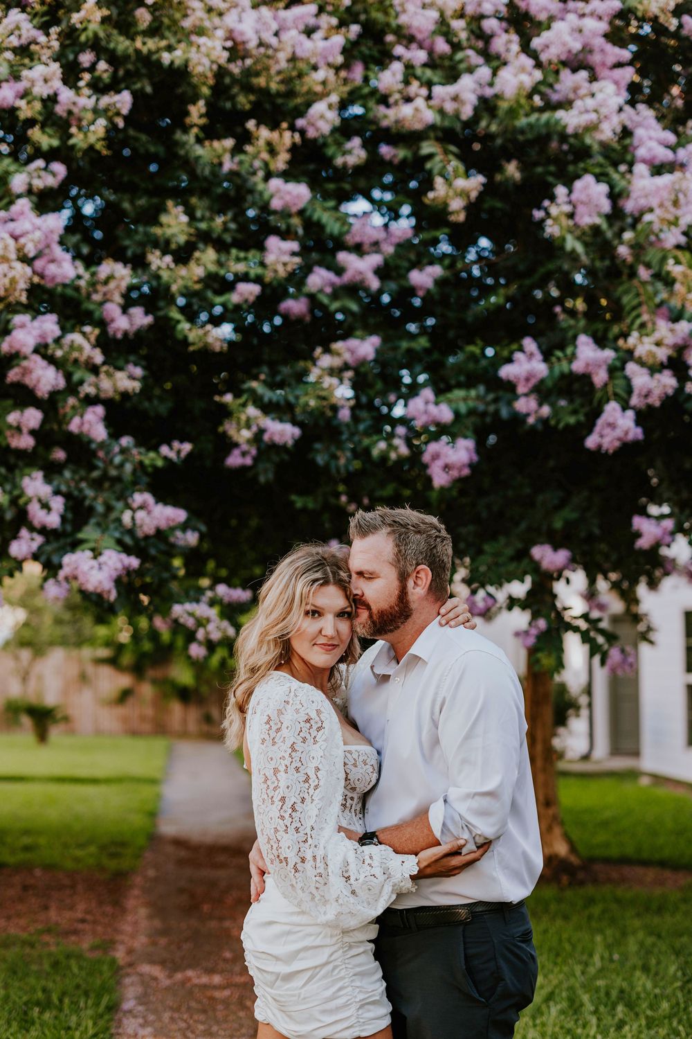 Couple embraces under blooming pink cherry blossom trees in romantic outdoor setting.