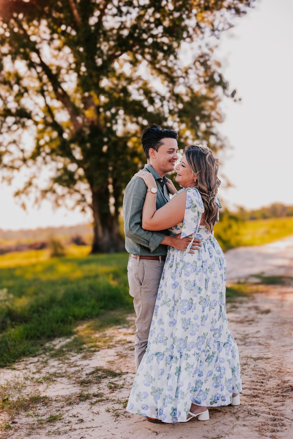 A couple embracing on a dirt path during golden hour with trees in background.