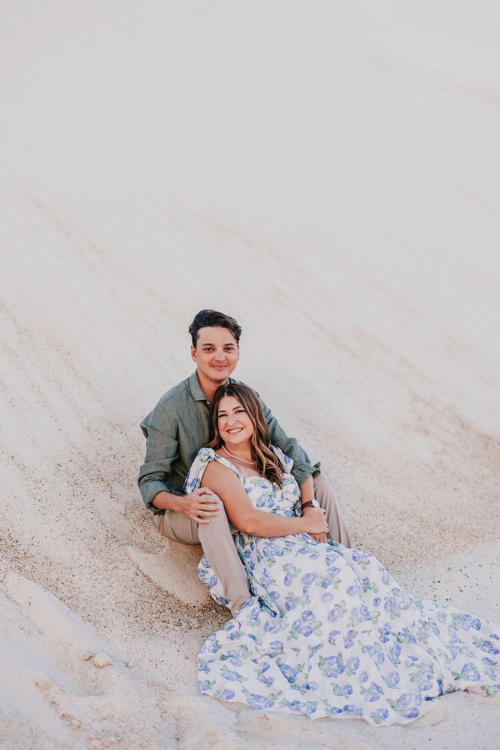 A couple poses playfully on white sand during a photo session.