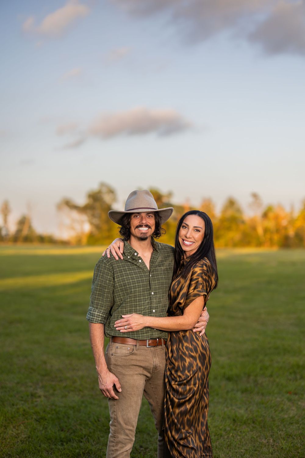 A couple embraces in casual attire during golden hour in an open field.