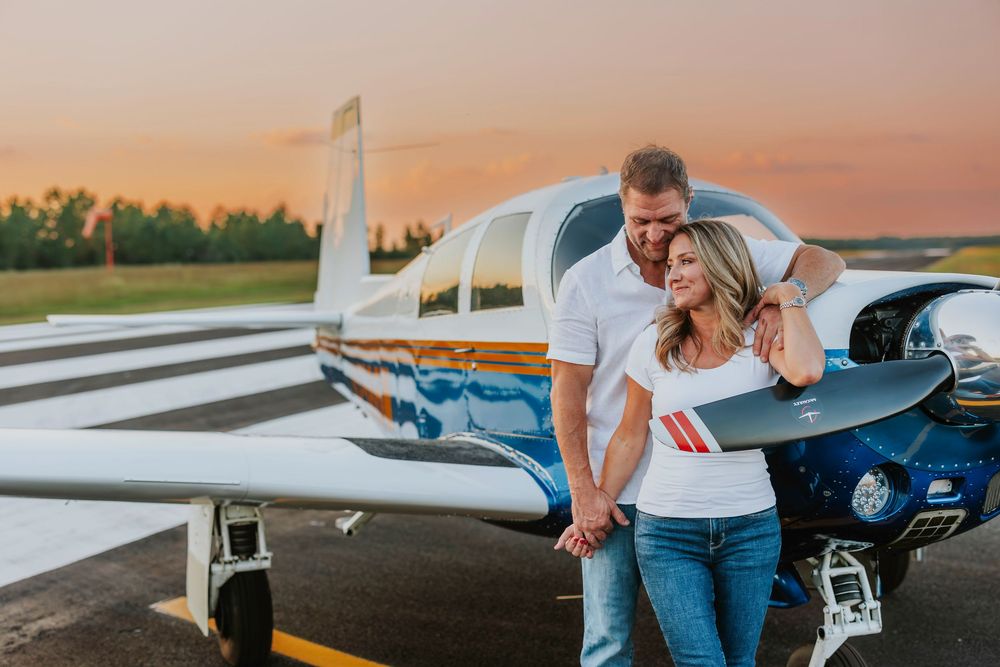 Romantic couple embracing next to parked aircraft on runway at dusk.