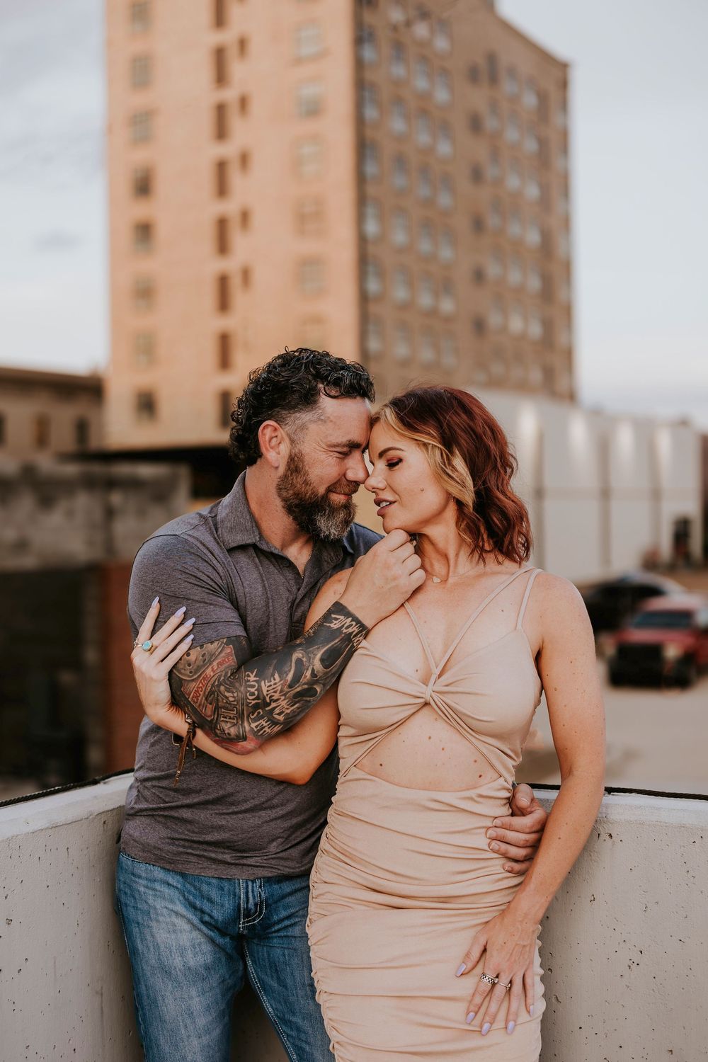 A romantic couple shares tender moments in a peach-colored dress and grey shirt against an urban backdrop.