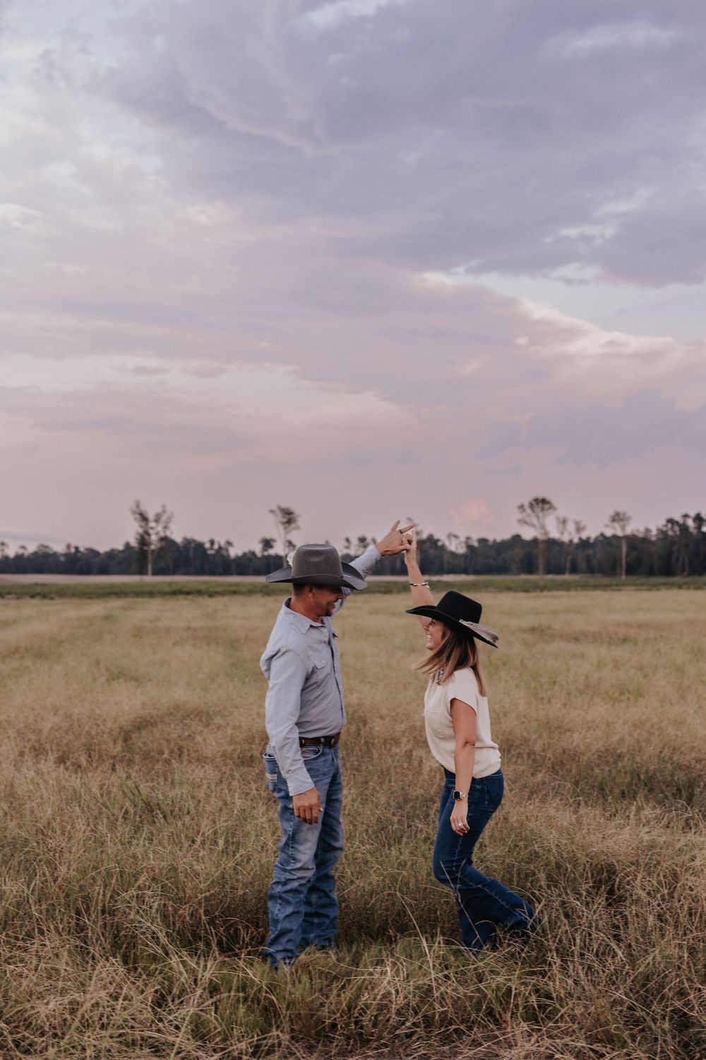 Couple in casual western wear playfully interacts in golden field at sunset.