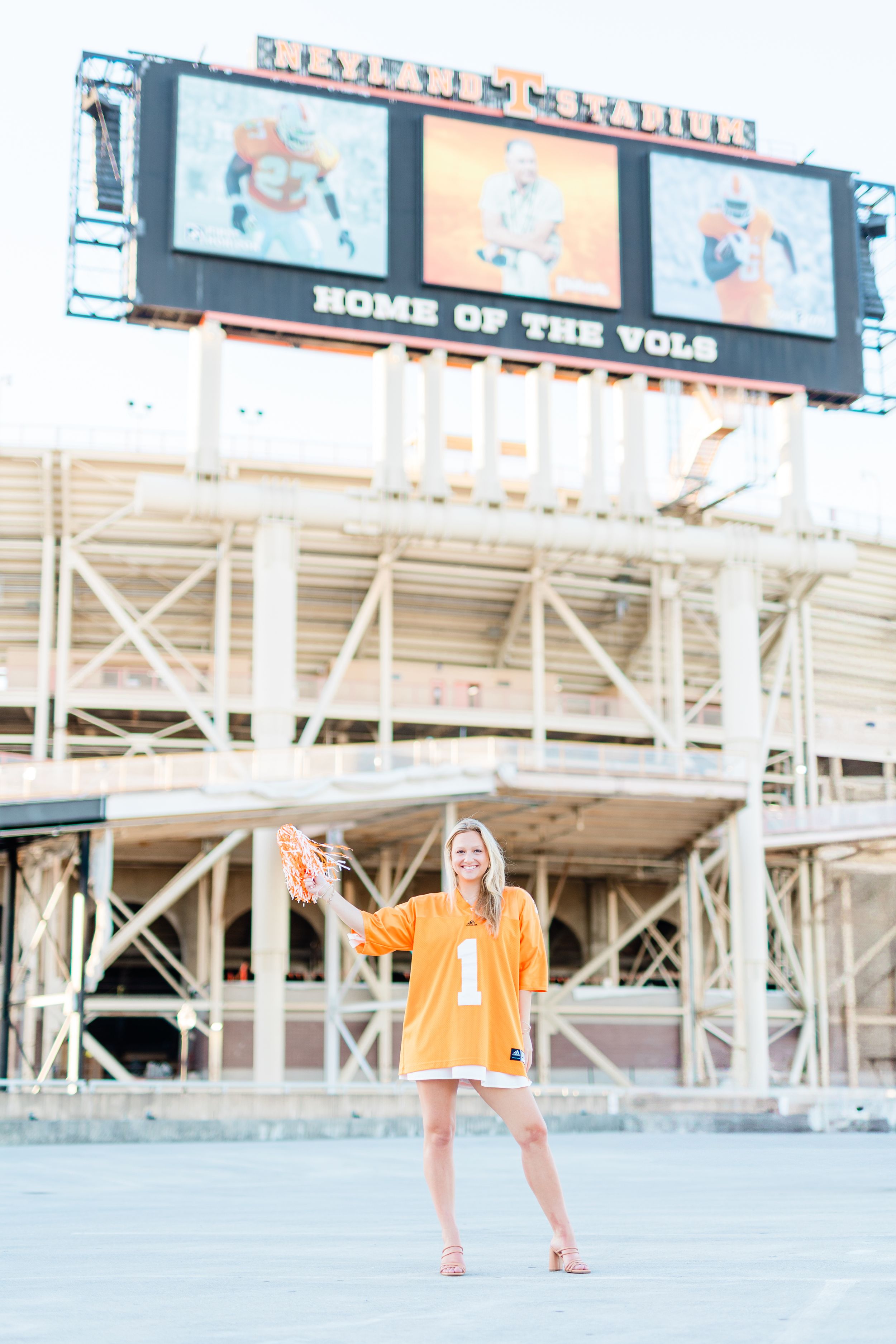People in orange outfits stand in front of a sports stadium with signage and bleachers visible in the background.