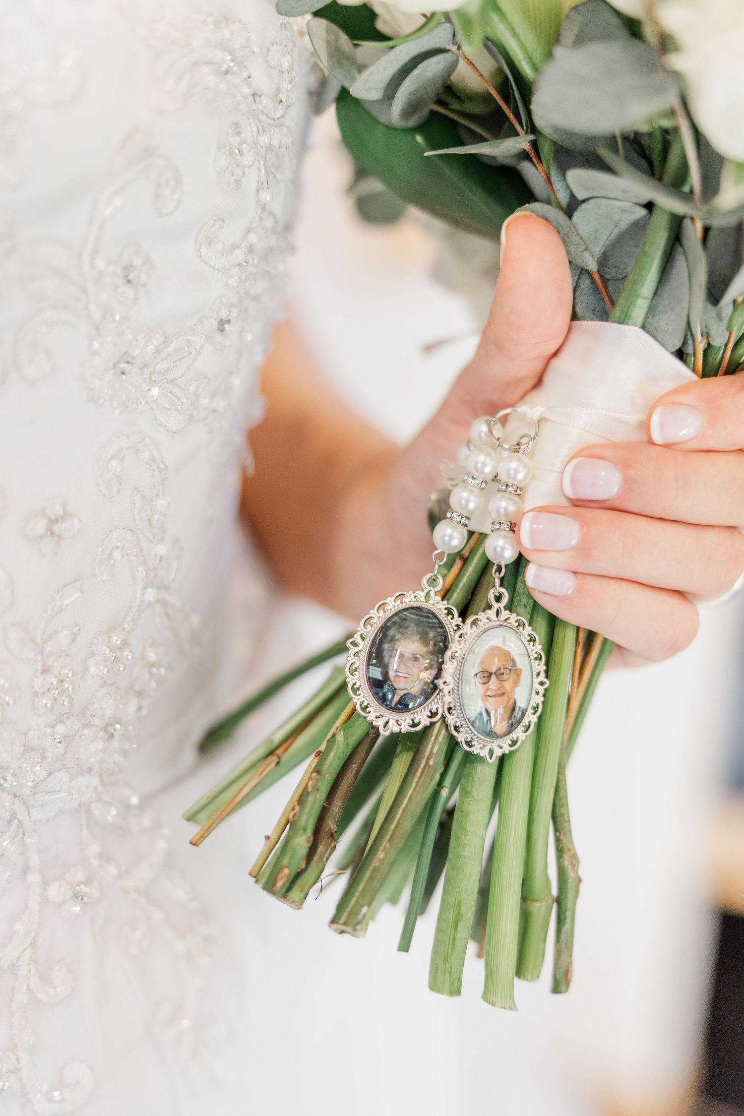 A bridal bouquet stem is decorated with a vintage-style rhinestone brooch and white lace ribbon.