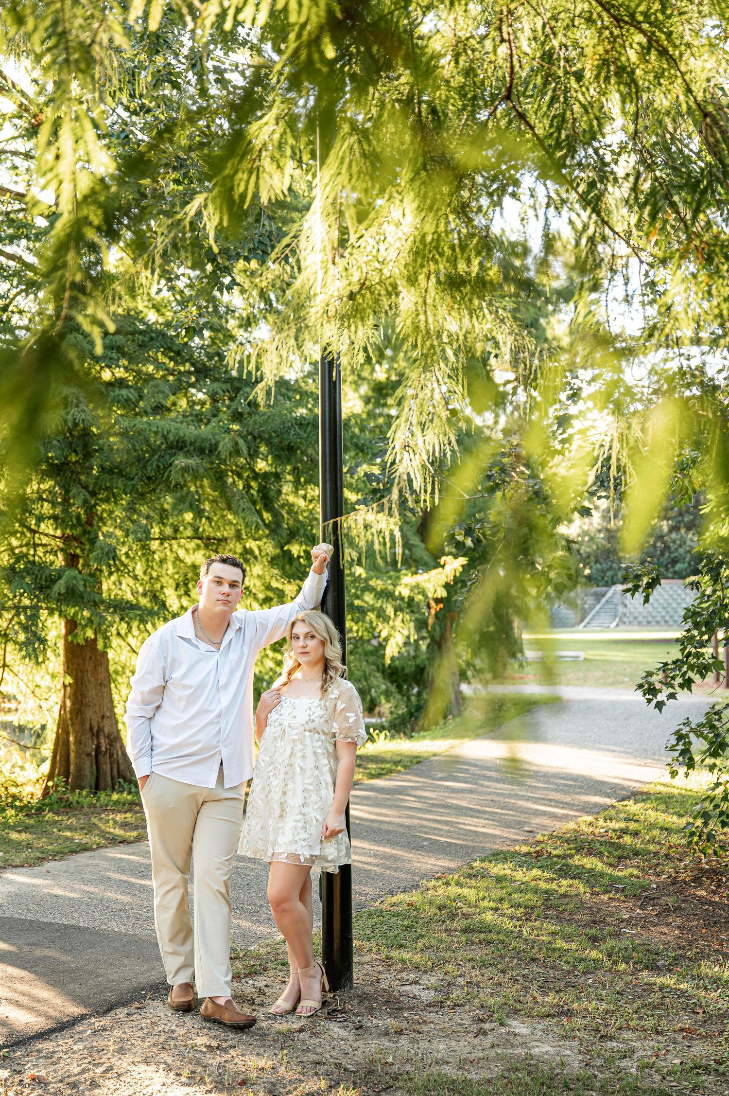 A couple poses beneath hanging moss in a sun-drenched park setting.