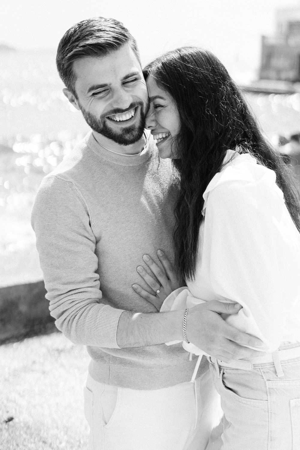 Black and white photo of a romantic couple embracing and laughing together outdoors in casual sweaters.