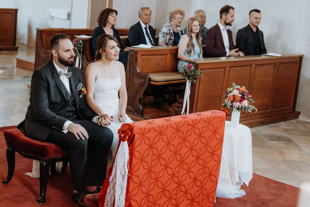 Church pews with orange and white decorations during wedding ceremony.