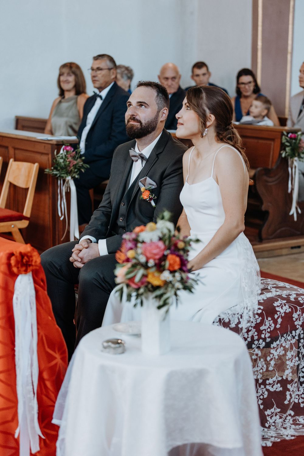Wedding ceremony seating arrangement in church with white and orange decorative elements.