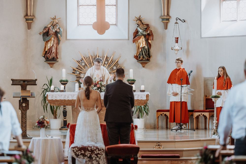 Church altar decorated for wedding ceremony with religious artwork and white decor.