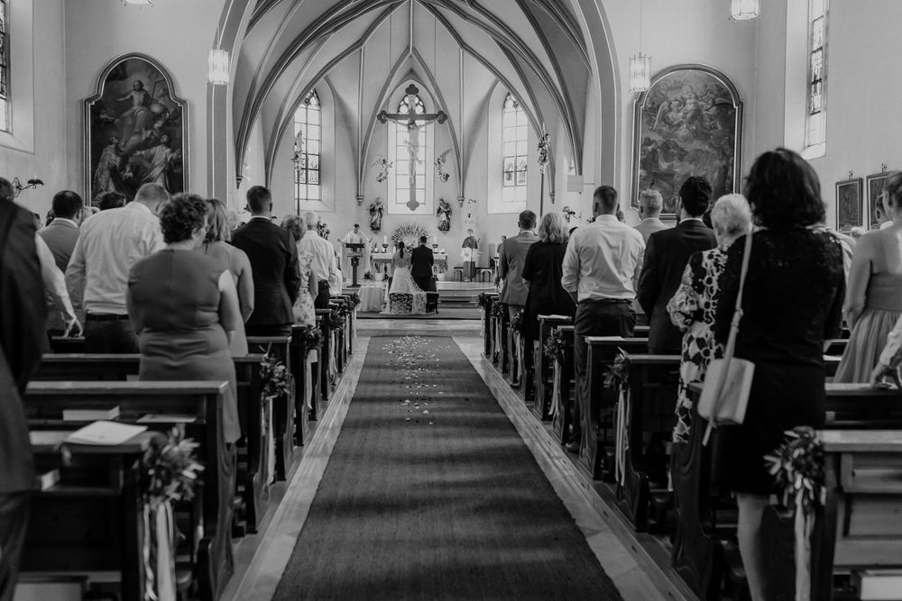 Wide angle black and white view of church aisle during wedding ceremony.