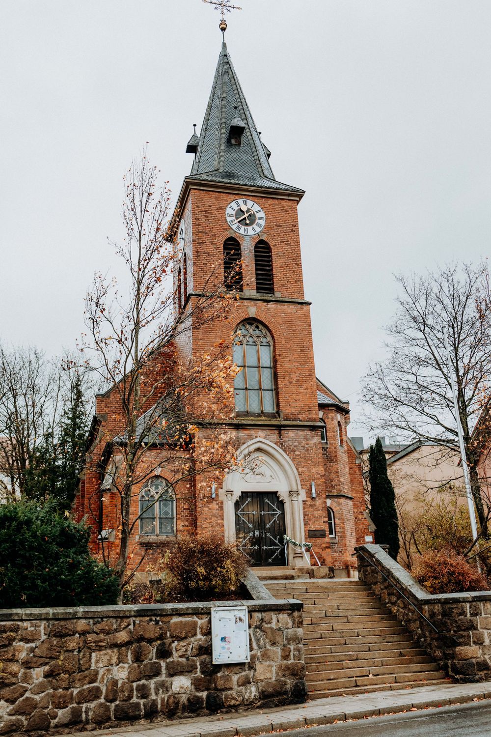 Historic red brick church with tall spire and stone foundation on hillside.