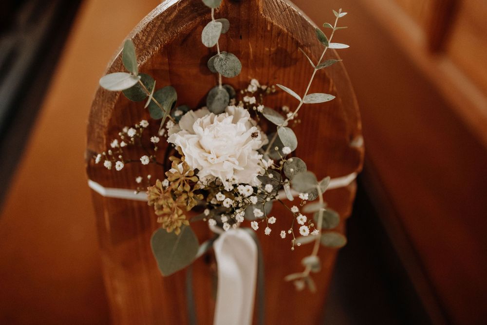 Delicate white and pink floral wedding decorations with eucalyptus leaves arranged on wooden church pews.
