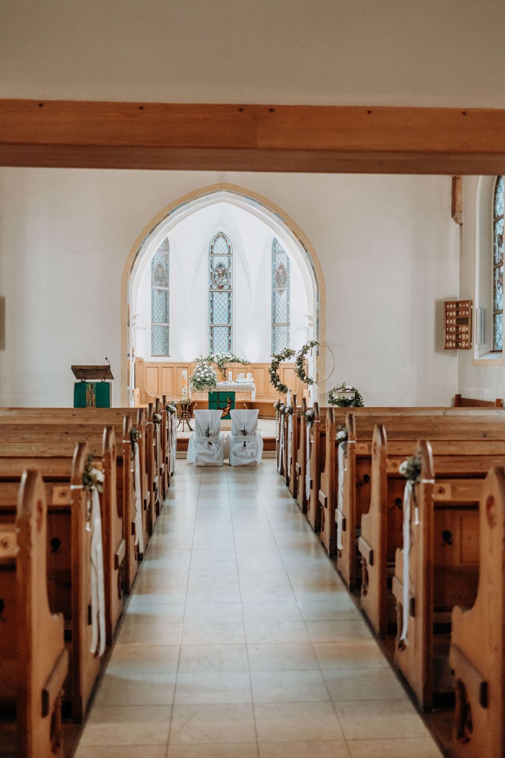 Sunlit church interior with wooden pews leading to arched altar area.