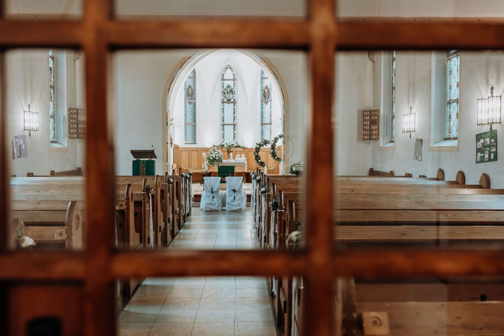 Interior view of empty church sanctuary with wooden pews and stained glass windows.