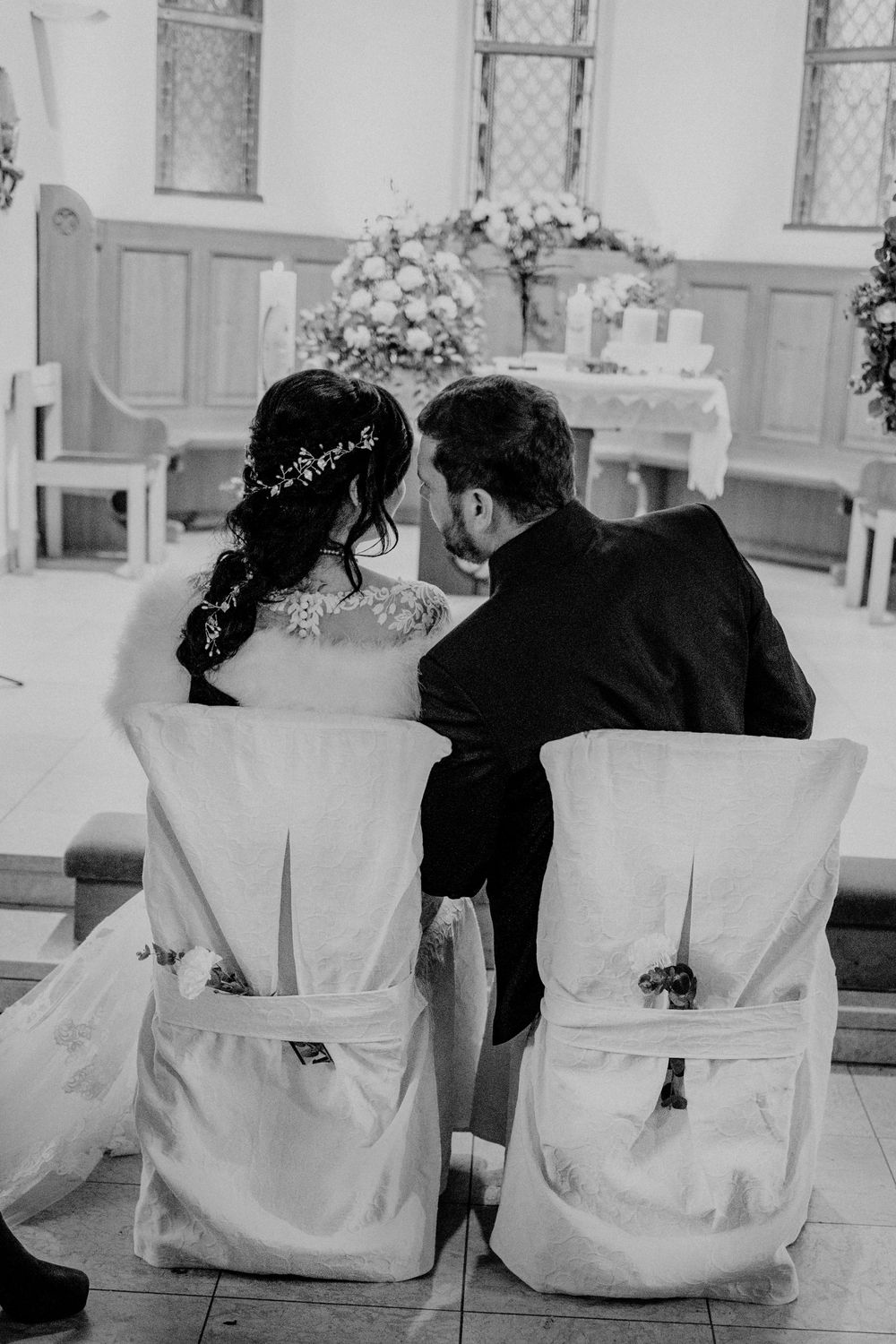 Row of white decorated chairs with floral arrangements in church setting.