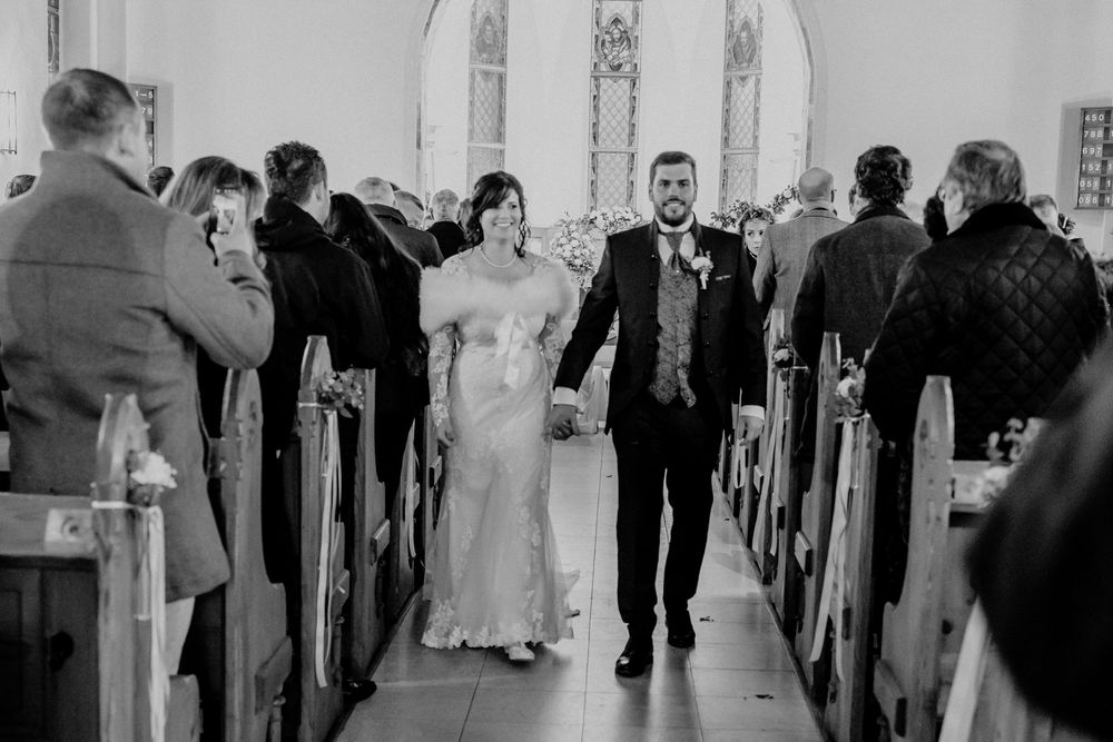 Black and white photo of wedding ceremony inside traditional church with wooden pews.