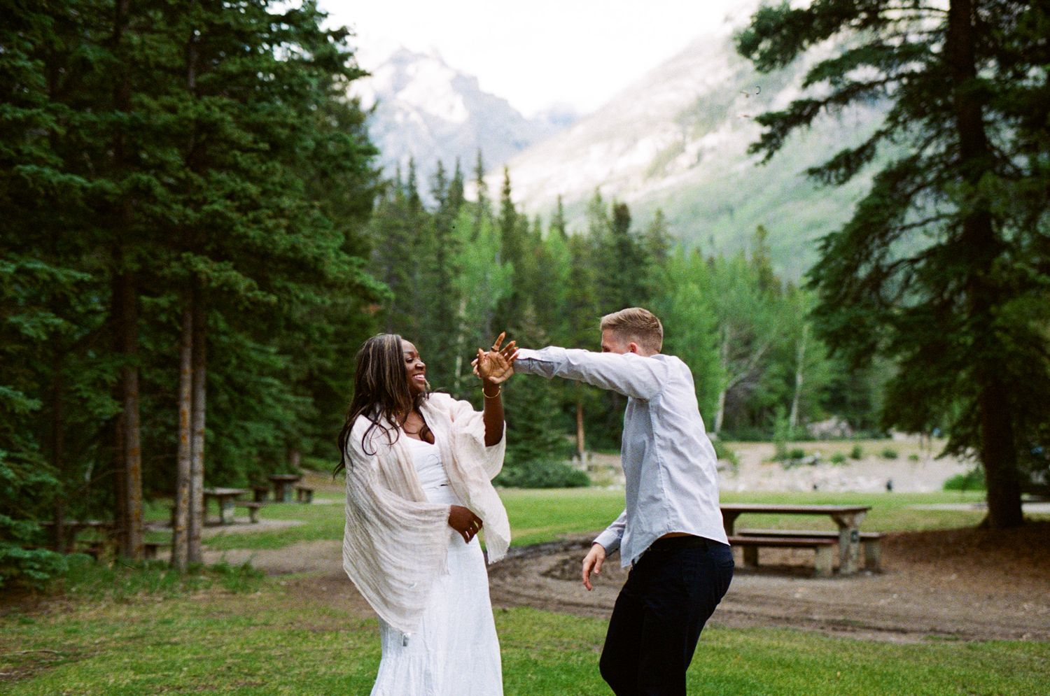 35 mm film photo of Bride and Groom laughing and spinning each other around in a campground in Banff National Park