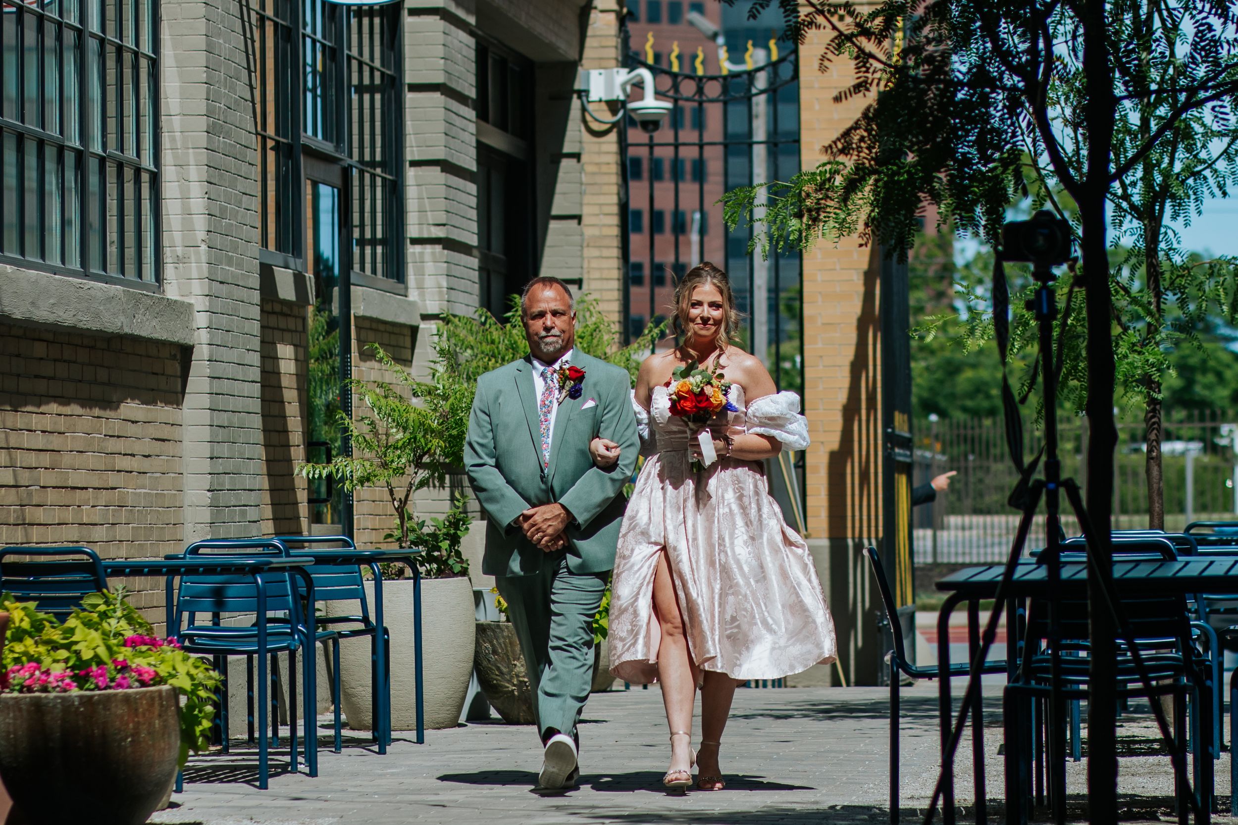 A couple sits and chats on a bench outside a brick building on a sunny afternoon.