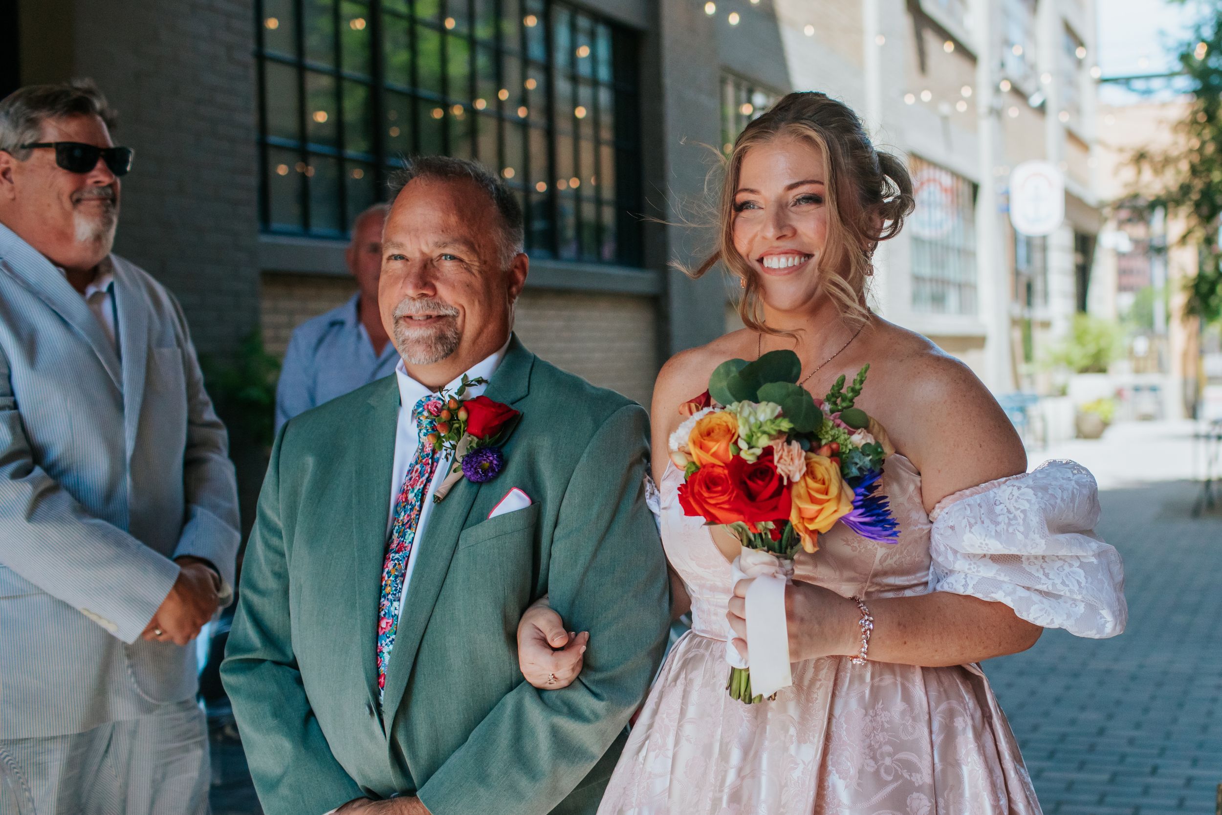 Wedding party members in green and white attire pose together outdoors.
