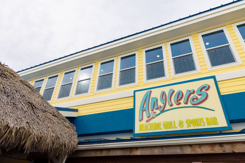 Yellow and blue exterior facade of a coastal restaurant with thatched roof details and outdoor dining area.