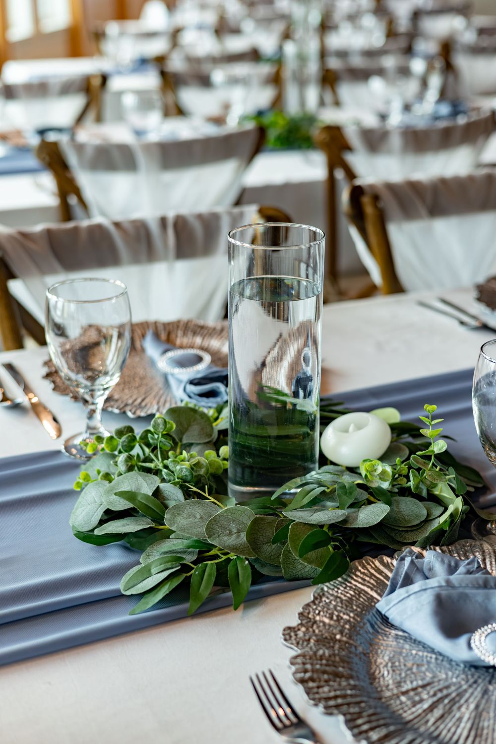 Elegant wedding table settings with greenery garlands, white candles, and metallic charger plates.