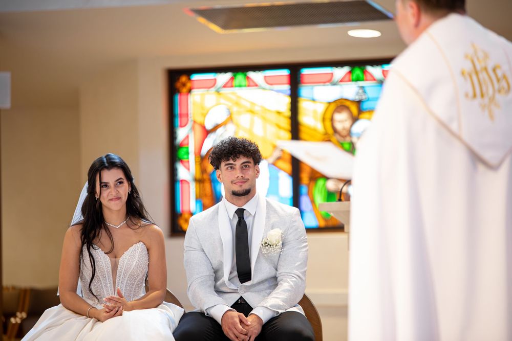 A couple shares an intimate moment during their wedding ceremony in a church with stained glass windows.